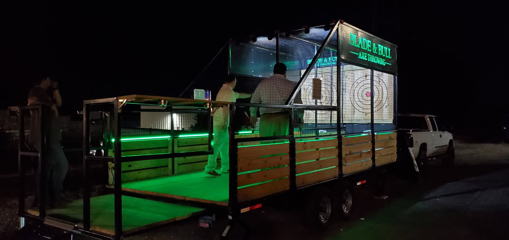 Our mobile axe-throwing trailer lit up at an evening event, with its previous Blade and Bull signage